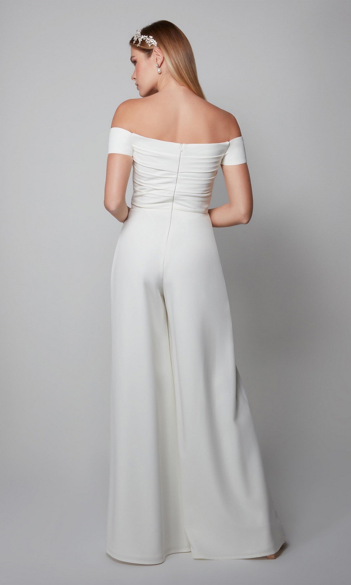 A woman stands with her back to the camera, wearing the Alyce 70014 Long Formal Jumpsuit and a decorative headpiece, against a plain gray background.